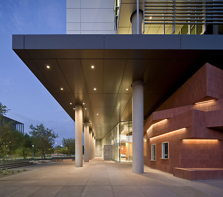 KGM-Lighting-Designer-Arizona-State-University-School-of-Earth-and-Science-Exploration-Exterior-Walkway - Detail view of the northwest at dusk looking towards the entry plaza that incorporates a variety of seating, gathering and landscaped areas with unique stone slab benches (shown in the foreground). The exterior materials reflect the clarity of the building’s organization as well as its dynamic and kinetic composition.